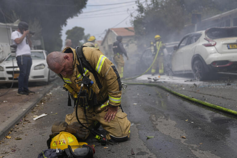 An Israeli firefighter kneels to recompose after he and his colleagues extinguished cars set on fire by a rocket fired from the Gaza Strip in Ashkelon, Israel, Monday, Oct. 9, 2023.