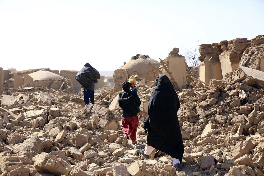 In this handout photo released by Save the Children, An Afghan woman with her children walk amid debris after a powerful earthquake in Herat province, western of Afghanistan, Sunday, Oct. 15, 2023.