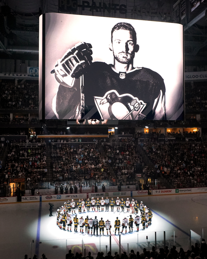 The Pittsburgh Penguins and Anaheim Ducks gather at center ice, before an NHL hockey game in Pittsburgh, Monday, Oct. 30, 2023, to honor former Penguin player Adam Johnson, shown on the scoreboard, who died in a "freak accident" while playing in an English hockey league game. (AP Photo/Gene J.