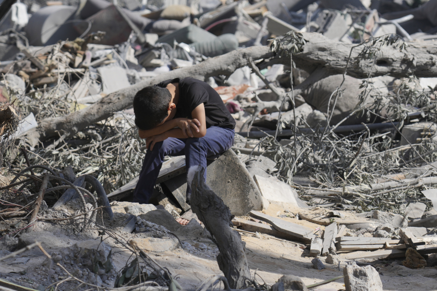 A Palestinian boy sits on the rubble of the building destroyed in an Israeli airstrike in Bureij refugee camp Gaza Strip, Wednesday, Oct. 18, 2023.