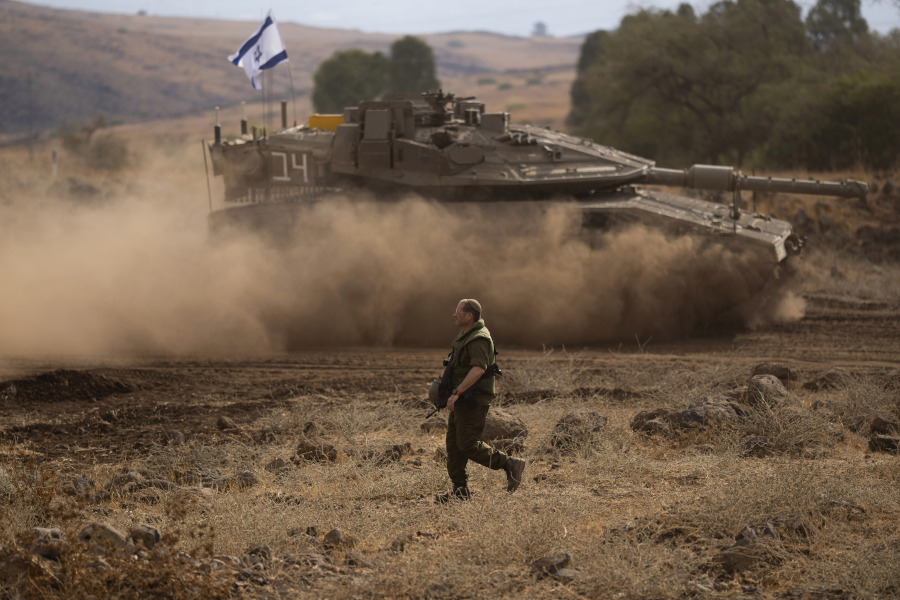 An Israeli soldier walks in front of a moving tank with an Israeli flag on the top in a staging area near the Israeli border with Lebanon, on Sunday, Oct. 15, 2023.