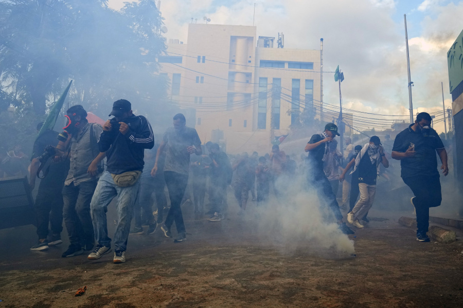 Protesters take cover from tear gas fired by riot police during a demonstration in solidarity with the Palestinian people in Gaza, near the U.S. embassy in Aukar, a northern suburb of Beirut, Lebanon, Wednesday, Oct. 18, 2023. Hundreds of angry protesters are clashing with Lebanese security forces in the Lebanese suburb Aukar near the United States Embassy.