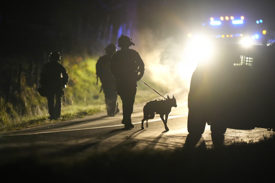 A member of law enforcement walks with a police dog outside a property on Meadow Road in Bowdoin, Maine, Thursday, Oct. 26, 2023. Hundreds of heavily armed police and FBI agents searched intensely for Robert Card, an Army reservist authorities say fatally shot a number of people at a bowling alley and a bar Wednesday.