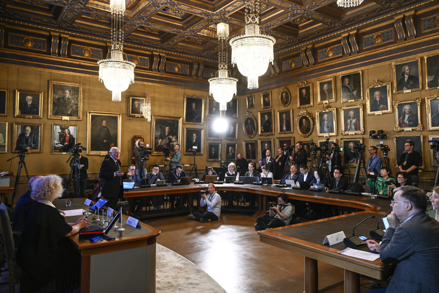Mats Larsson, member of the Royal Academy of Sciences, standing at left, speaks during the announcement of the winner of the 2023 Nobel Prize in Physics, at the Royal Academy of Sciences, in Stockholm, Tuesday, Oct. 3, 2023. The Nobel Prize in physics has been awarded to Pierre Agostini, Ferenc Krausz and Anne L'Huillier for looking at electrons in atoms by the tiniest of split seconds.
