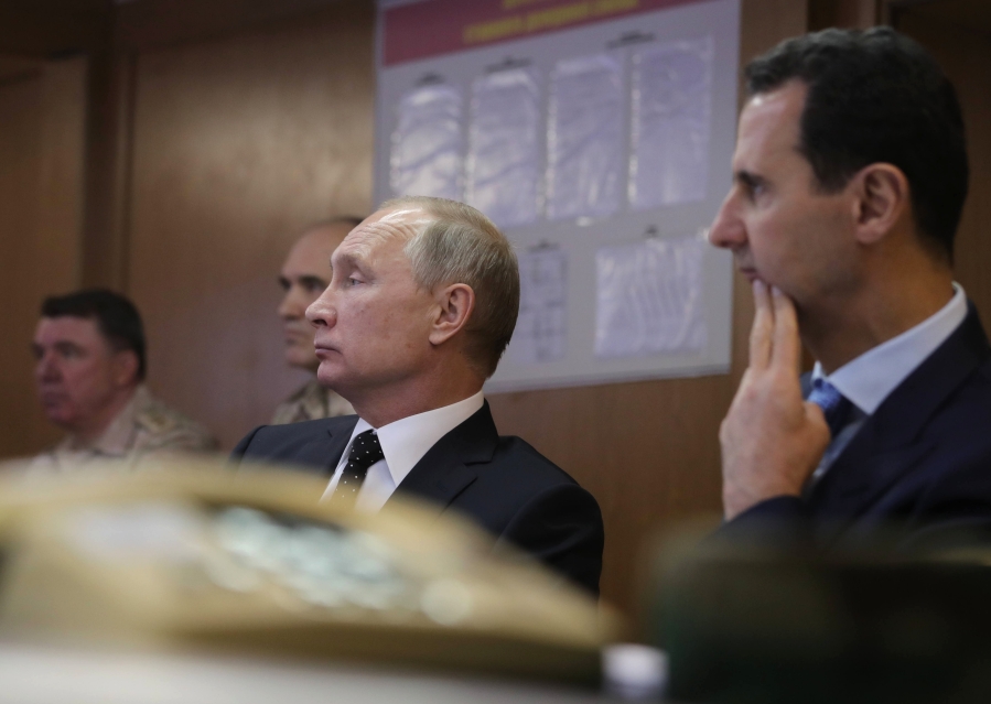 FILE - Russian President Vladimir Putin, center, and Syrian President Bashar Assad, 2nd right, meet with military personnel at the Hemeimeem air base in Syria, on Dec. 11, 2017. The Russian military intervention in Syria allowed Syrian President Bashar Assad's government to reclaim control over most of the country and helped expand Moscow's clout in the Middle East.