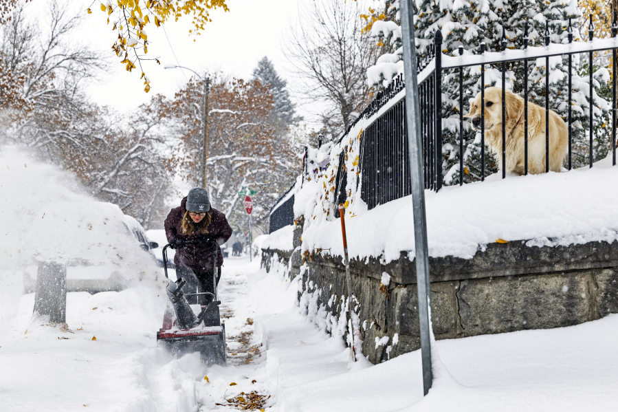A person clears a snow-covered sidewalk, Wednesday, in Helena, Mont. The first major snowstorm of the season dropped up to a foot of snow in the Helena area by Wednesday morning, canceling some school bus routes.