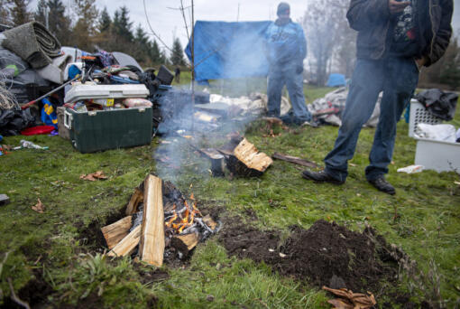 Smoke billows from a campfire under cold conditions as Vancouver resident Greg Wilson, background left, who is not a resident of the Burnt Bridge Creek encampment, helps his friend set up his gear in the new location Wednesday morning.