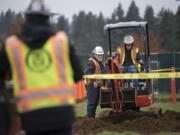 Tapani&rsquo;s John Jordan, left, looks on as Evergreen High School junior Isaiah Florendo, 16, gives a mini-excavator a try on Thursday morning.