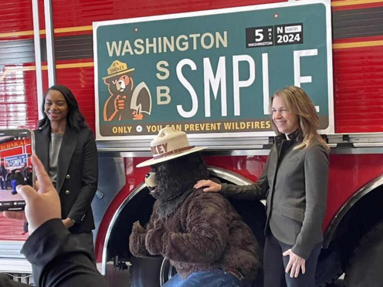 Commissioner of Public Lands Hilary Franz, right, state Sen. T&rsquo;wina Nobles and Smokey Bear pose in front of a proposed speciality license plate Monday in a Pierce County fire station.