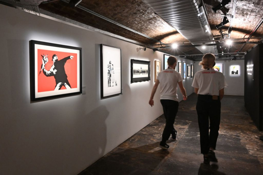 Gallery assistants walk past &ldquo;Love Is In The Air (Flower Thrower)&rdquo; 2003 (left) by British street artist Banksy at a photocall for the opening of an unauthorized exhibition &ldquo;The Art of Banksy&rdquo; in London on May 18, 2021.