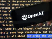 The OpenAI logo appears on a mobile phone in front of a screen showing a portion of the company website in this photo taken on Tuesday, Nov. 21, 2023 in New York.