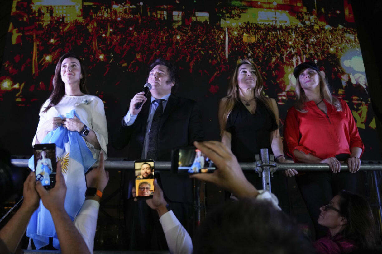 Presidential candidate of the Liberty Advances coalition Javier Milei speaks to supporters outside his campaign headquarters after winning the runoff election in Buenos Aires, Argentina, Sunday, Nov. 19, 2023. At left is his running mate Victoria Villarruel, second from right his girlfriend Fatima Florez and at right his sister Karina Milei.