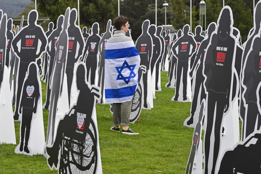 A supporter of Israel walks amongst cutout cardboard effigies, representing Israeli hostages, during a protest outside Parliament House in Canberra, Australia, Tuesday, Nov. 28, 2023.