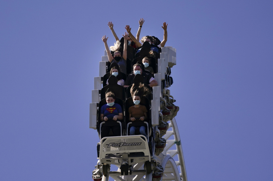 FILE - Visitors wearing masks ride on a roller coaster at Six Flags Magic Mountain on its first day of reopening to members and pass holders in Valencia, Calif., on April 1, 2021. Cedar Fair and Six Flags Entertainment Corp. are merging, creating an expansive amusement park operator with operations spread across 17 states and three countries. (AP Photo/Jae C.