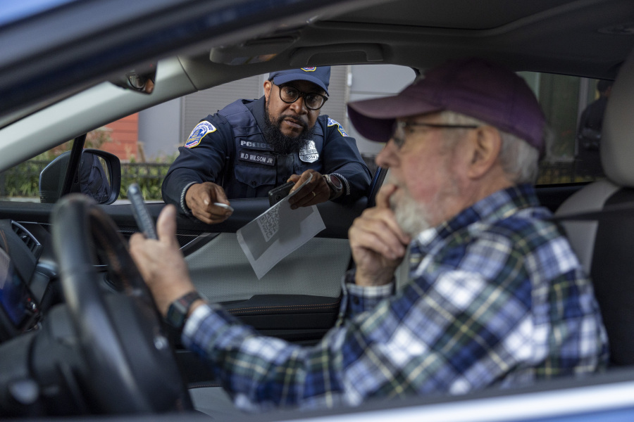 Metropolitan Police Department officer Muhammad Lewis explains to Nils Bruzelius how to use a Tile tracker during an event where police officers distributed mobile tracking devices for cars to drivers in an attempt to curb a rise in crime in Washington on Tuesday, Nov. 7, 2023.