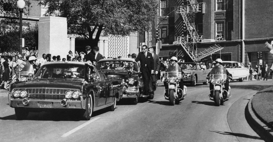 FILE - Seen through the foreground convertible&#039;s windshield, President John F. Kennedy&#039;s hand reaches toward his head within seconds of being fatally shot, as first lady Jacqueline Kennedy holds his forearm, as the motorcade proceeds along Elm Street past the Texas School Book Depository, Nov. 22, 1963, in Dallas. The 60th anniversary of President Kennedy&#039;s assassination, marked on Wednesday, Nov. 22, 2023, finds his family, and the country, at a moment many would not have imagined in JFK&#039;s lifetime. (AP Photo/James W.