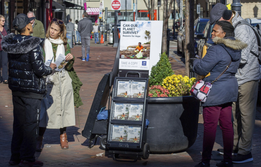 A woman shares Jehovah&rsquo;s Witnesses&rsquo; literature with a passerby Nov. 13 in downtown Pittsburgh. Jehovah&rsquo;s Witnesses regularly distribute literature in public places and do door-to-door evangelism, but for the first time in more than a century, their congregations will not be regularly tracking their hours in ministry.