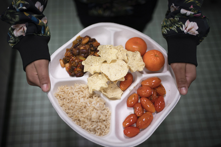 A seventh grader carries her plate which consists of three bean chili, rice, mandarins, cherry tomatoes and baked chips during her lunch break Feb. 10 at a public school in the Brooklyn borough of New York.