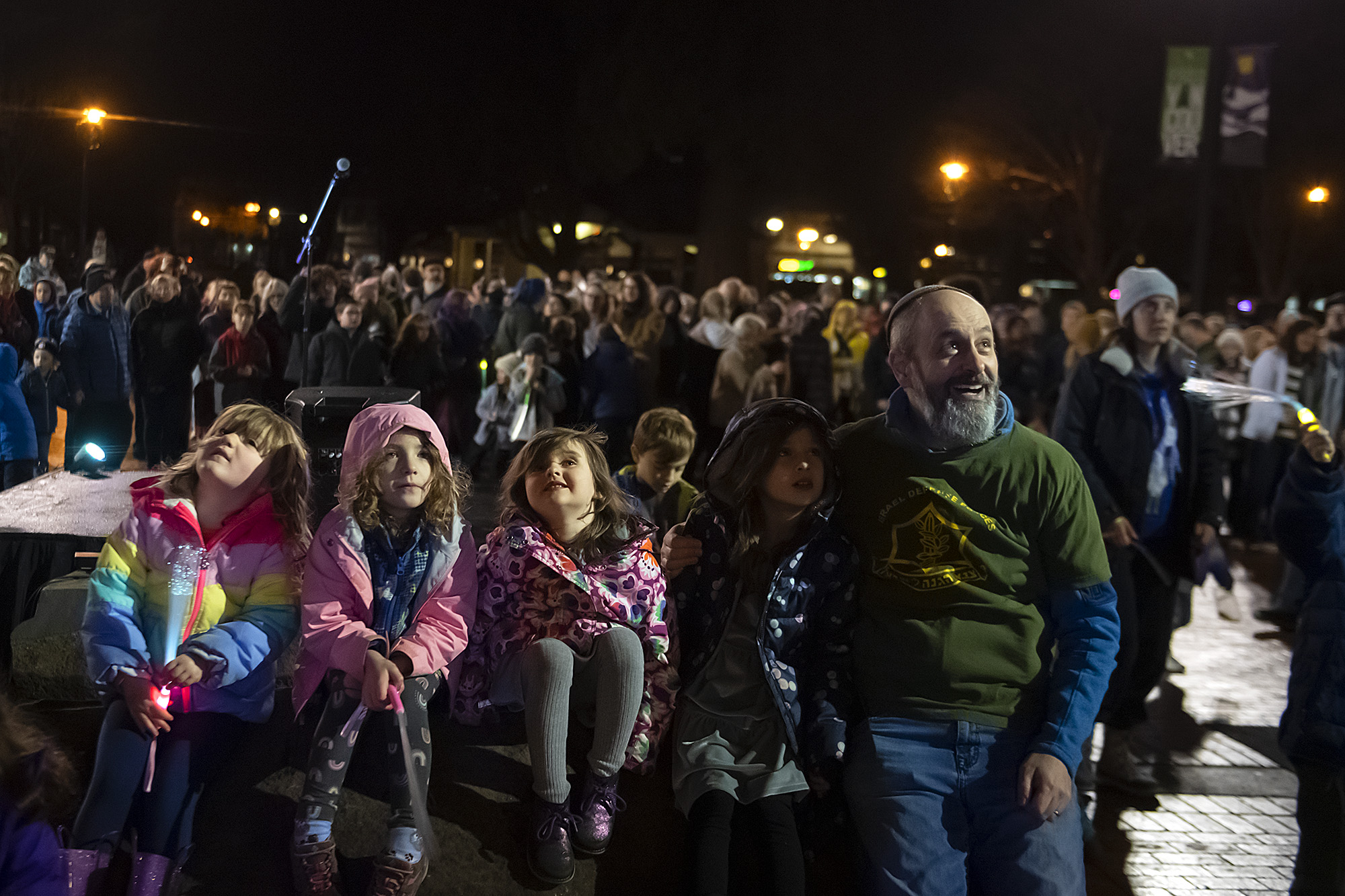 Participants look upward as they wait for Rabbi Shmulik Greenberg to toss chocolate coins for the children from his cherry picker basket while celebrating the beginning of Hanukkah at Esther Short Park on Thursday evening, Dec. 7, 2023.