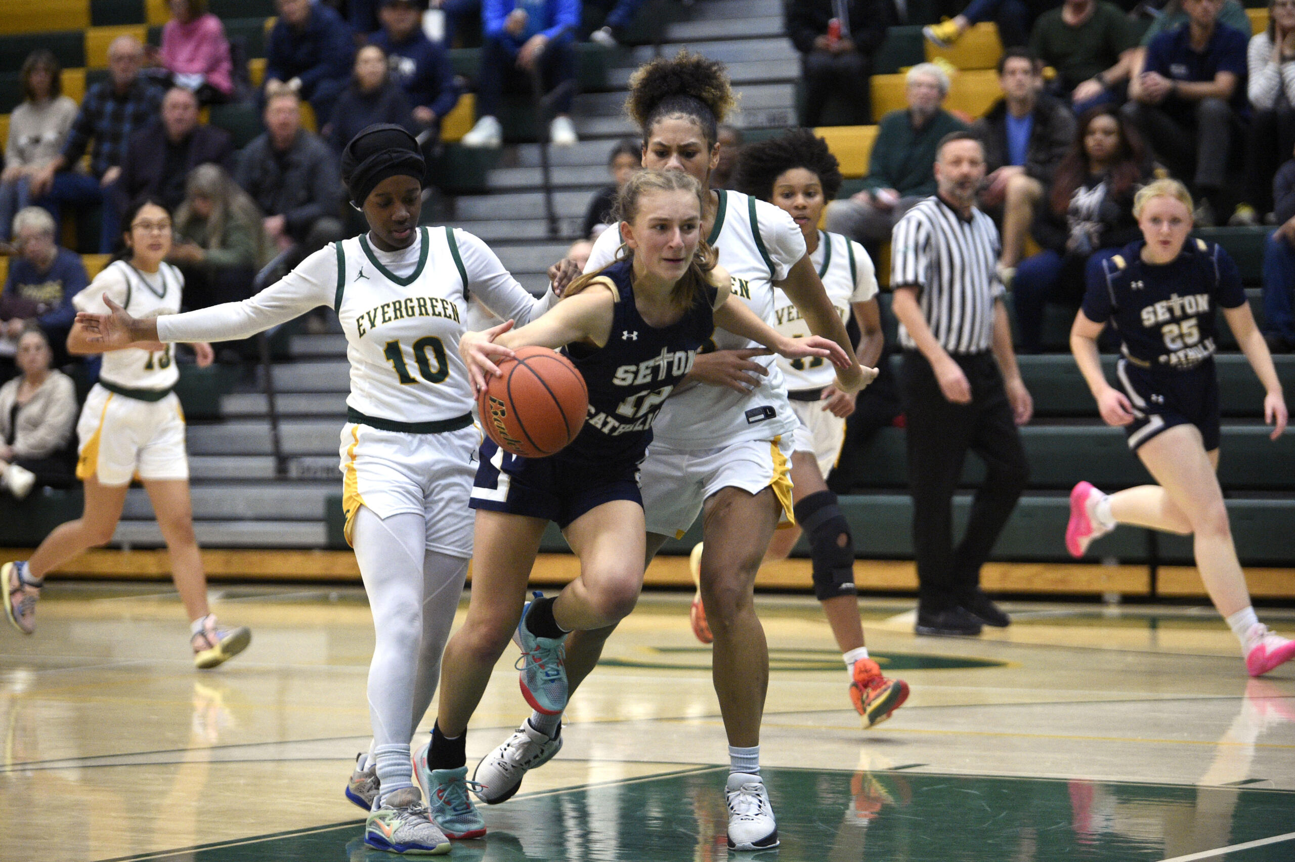Seton Catholic’s Remy Jenniges (12) goes between Evergreen defenders Fatima Juwara, left, and Alexis Echols, right, during a non-league girls basketball game on Tuesday, Dec. 5, 2023, at Evergreen High School.