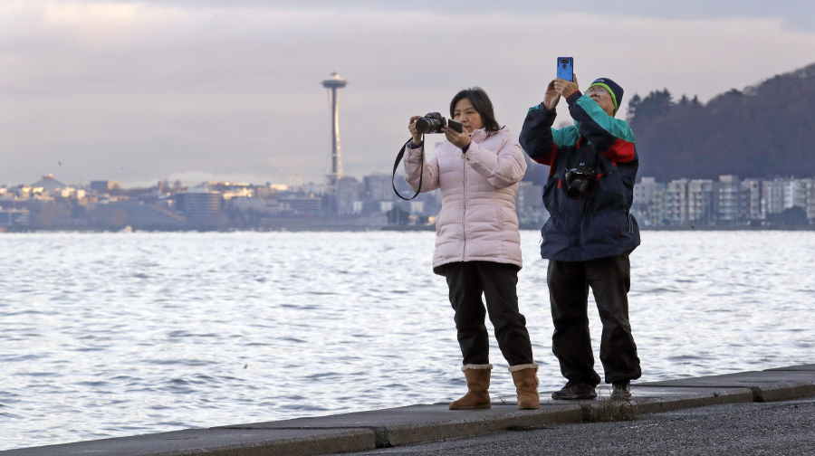 Anna Tsoi, left, and her husband, Tin Fuk, stand on a seawall and take photos of Puget Sound during an unusually high tide, often called a &ldquo;king tide,&rdquo; on Dec. 27, 2018, in Seattle.