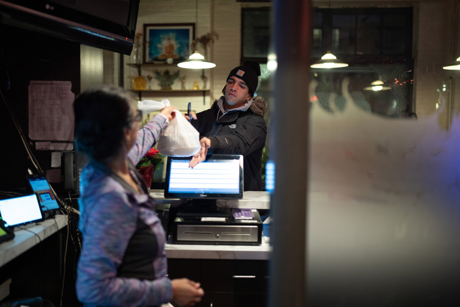 Sam Simonson hands a takeout order to a DoorDash delivery person at Sawatdee in Minneapolis on Thursday night, Dec. 14, 2023. Third party delivery food delivery services are a growing share of business at fast food restaurants and for other restaurants with cuisines that travel well, like the Thai menu at Sawatdee in Minneapolis, where they account for 30% of their business.