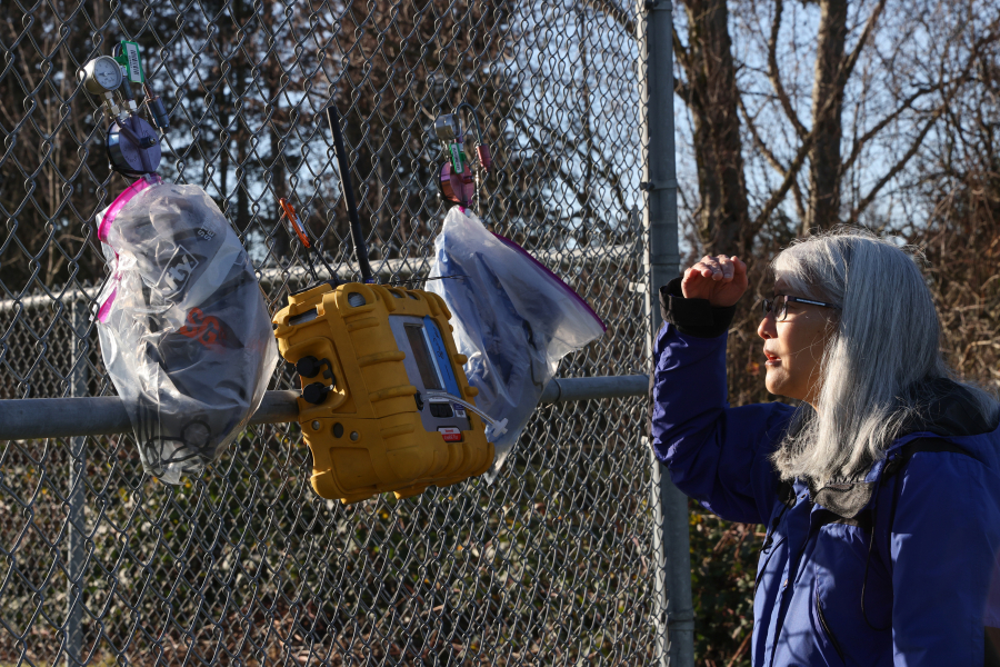 Scarlet Tang, communications manager for the Department of Ecology, Northwest region, looks at air quality monitoring devices tied to a fence outside the Conway Elementary school in Conway, Washington, on Wednesday, Dec. 20, 2023.
