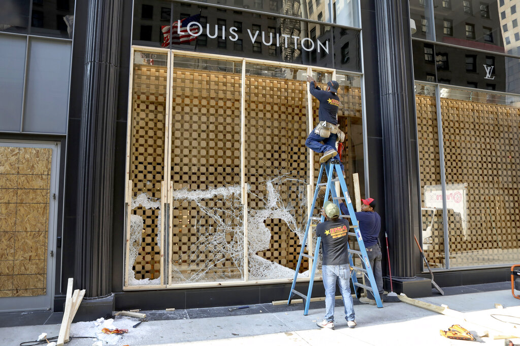 FILE - Workers begin to board up a display window at the Louis Vuitton store Monday, Aug. 10, 2020, after overnight vandals hit many high-end stores in Chicago. The Illinois Senate has a bipartisan plan to crack down on a recent spate of smash-and-grab retail thefts and the fencing that follows. Bill sponsor Western Springs Democratic Sen. Suzy Glowiak Hilton says smash-and-grab crimes not only result in product loss but terrorize employees and patrons and damage property.