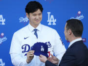 Los Angeles Dodgers' Shohei Ohtani, left, is handed a baseball cap by president of baseball operations Andrew Friedman during a news conference at Dodger Stadium Thursday, Dec. 14, 2023, in Los Angeles.