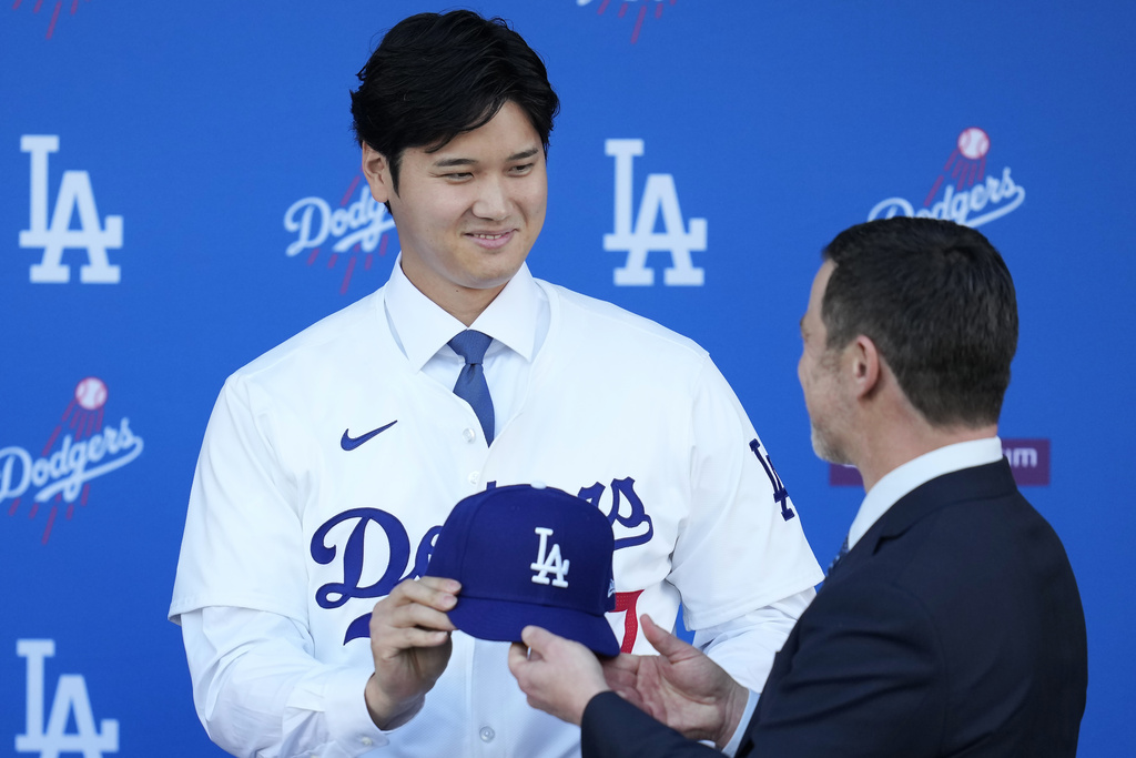 Los Angeles Dodgers' Shohei Ohtani, left, is handed a baseball cap by president of baseball operations Andrew Friedman during a news conference at Dodger Stadium Thursday, Dec. 14, 2023, in Los Angeles.