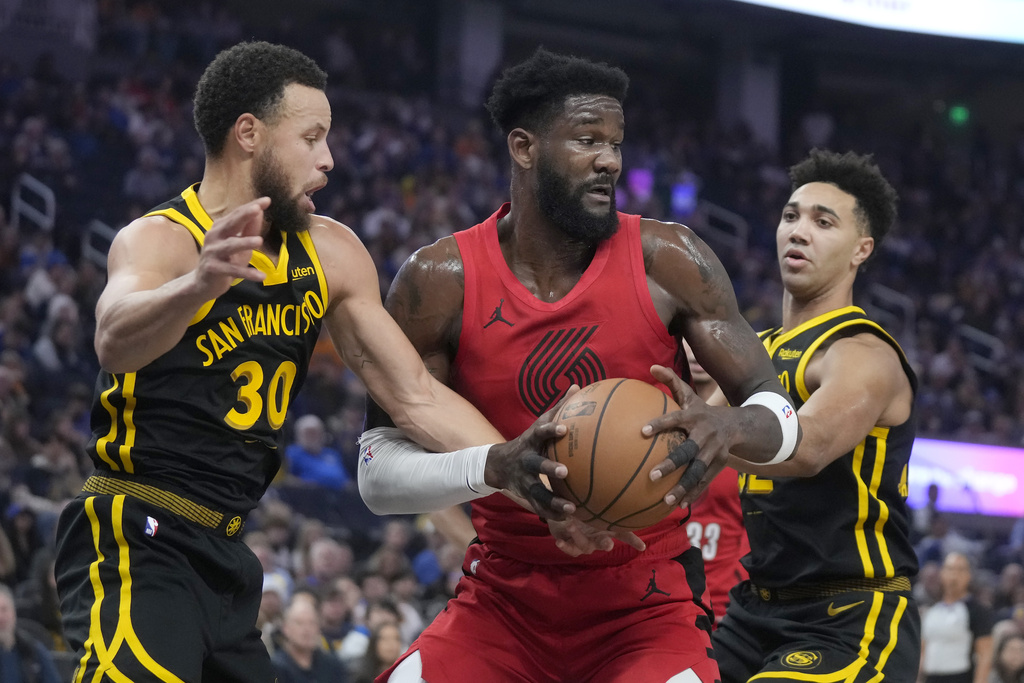 Portland Trail Blazers center Deandre Ayton, center, tries to turn toward the basket between Golden State Warriors guard Stephen Curry (30) and forward Trayce Jackson-Davis, right, during the first half of an NBA basketball game in San Francisco, Saturday, Dec. 23, 2023.