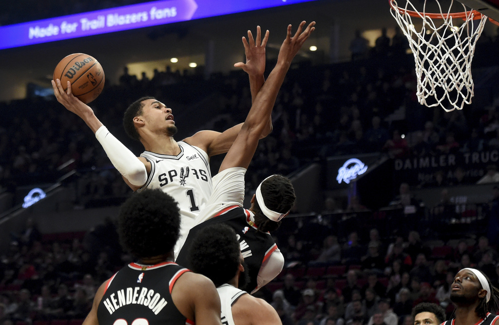San Antonio Spurs center Victor Wembanyama, left, drives to the basket against Portland Trail Blazers center Moses Brown, center, as forward Jerami Grant, right, watches during the first half of an NBA basketball game in Portland, Ore., Thursday, Dec. 28, 2023.