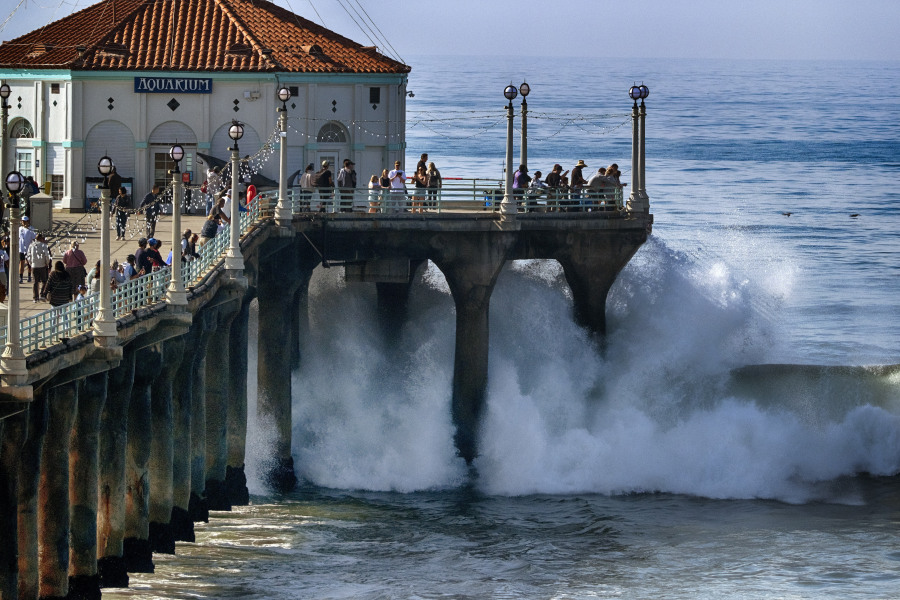 People watch as surf pounds the side of the pier in Manhattan Beach, Calif. on Thursday.