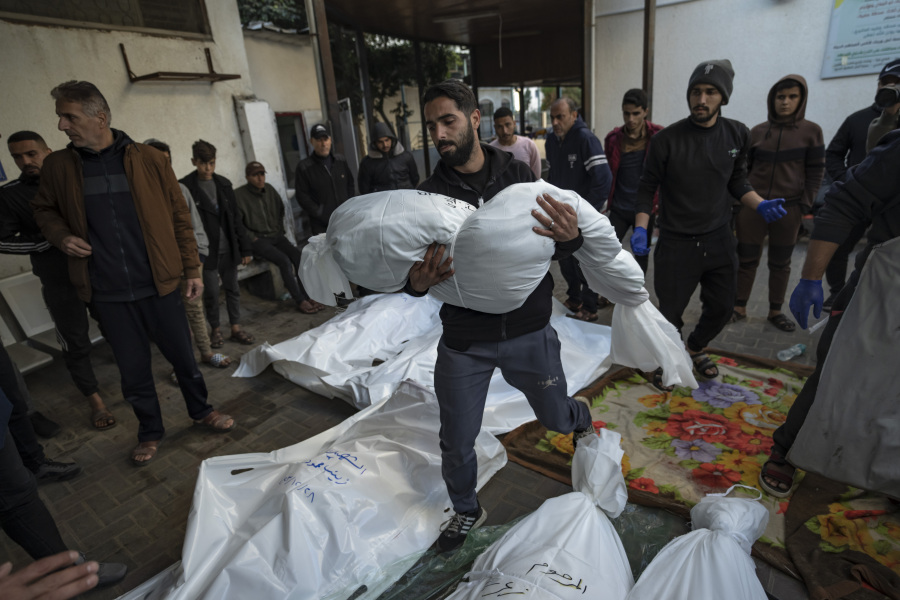 A Palestinian man carries the body of his relative killed in the Israeli bombardment of the Gaza Strip, outside a morgue in Rafah, southern Gaza, Friday, Dec. 29, 2023.
