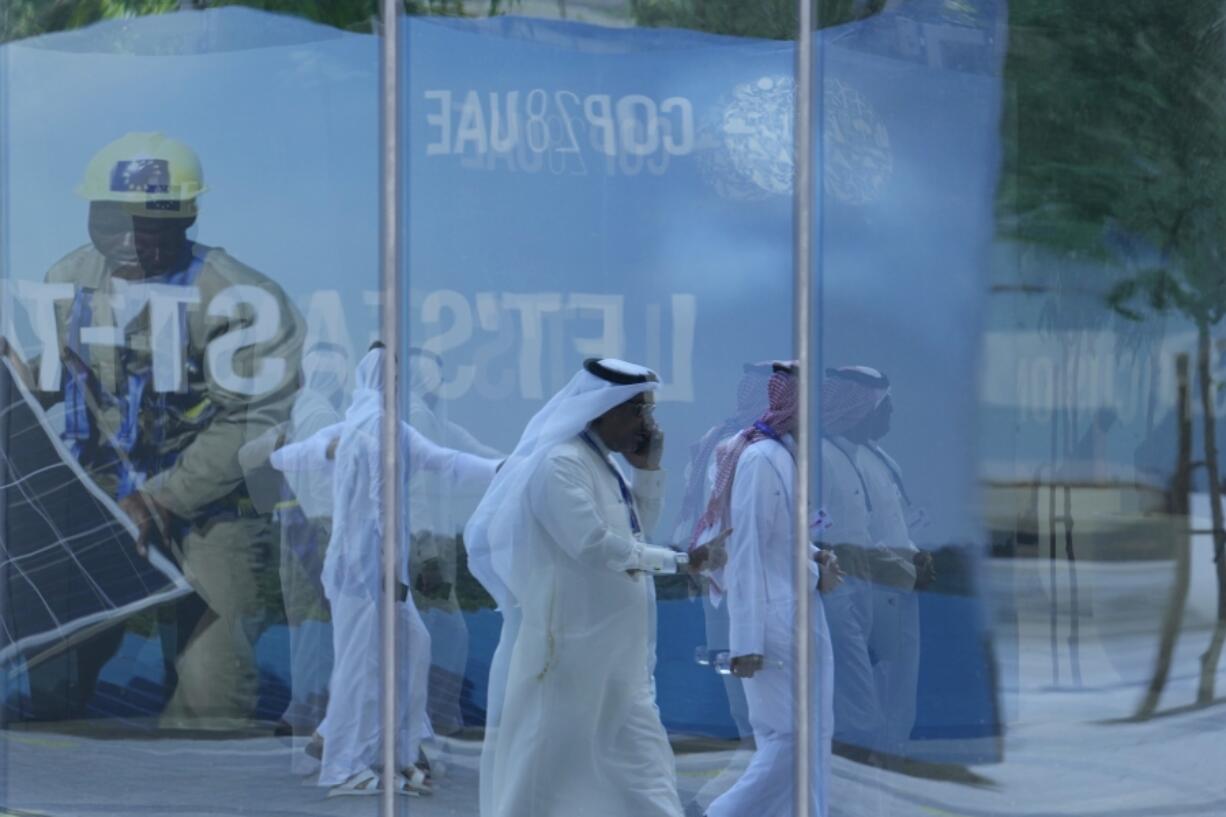 People walk near a sign for the COP28 U.N. Climate Summit, Tuesday, Nov. 28, 2023, in Dubai, United Arab Emirates.
