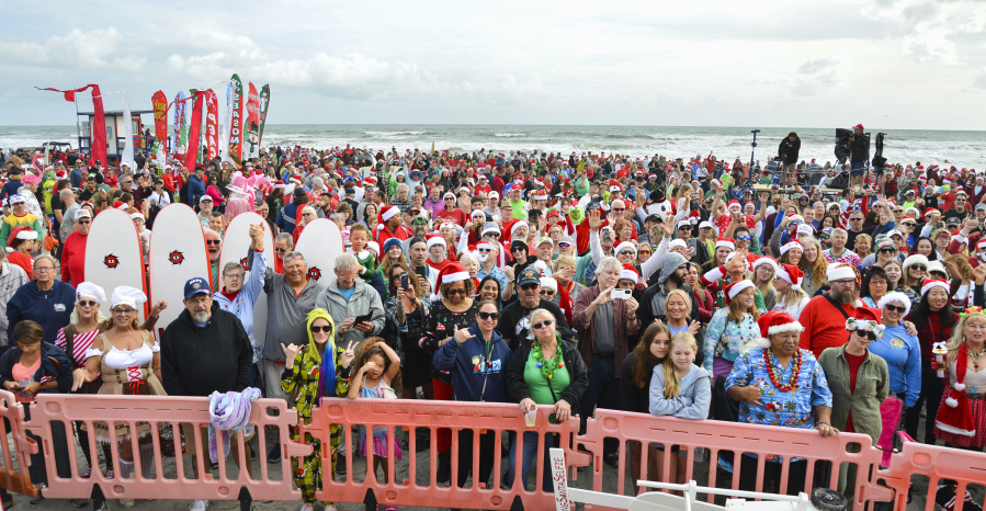 Crowds gather for the Surfing Santa event Christmas Eve morning in Cocoa Beach Fla., on Sunday, Dec. 24, 2023. The tradition started in 2009 when George Trosset and his son, George Jr., went surfing in a Santa suit and an elf costume on Christmas Eve. Friends found out about it and joined them the next year. The event grew each year and now in its 15th year the event attracts thousands and has become a fund raiser for the Florida Surf Museum and Grind for Life, an organization that provides financial assistance to cancer victims.