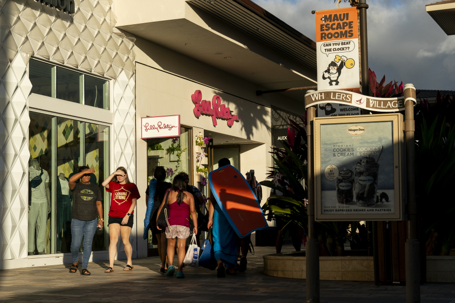 People walk by shops at the Whalers Village shopping mall, Wednesday, Dec. 6, 2023, in Lahaina, Hawaii. Residents and survivors still dealing with the aftermath of the August wildfires in Lahaina have mixed feelings as tourists begin to return to the west side of Maui.