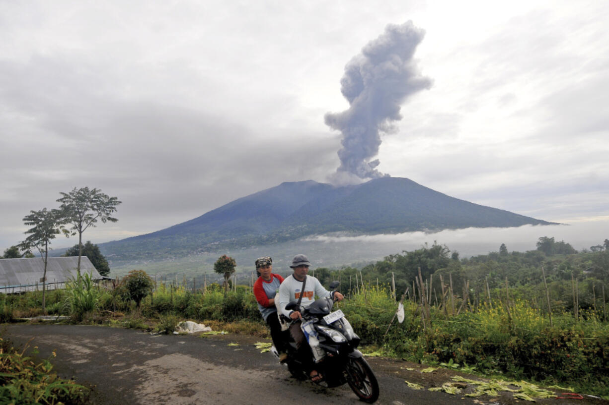 Motorists ride past by as Mount Marapi spews volcanic materials during its eruption in Agam, West Sumatra, Indonesia, Monday, Dec. 4, 2023. The volcano spewed thick columns of ash as high as 3,000 meters (9,800 feet) into the sky in a sudden eruption Sunday and hot ash clouds spread several miles (kilometers).