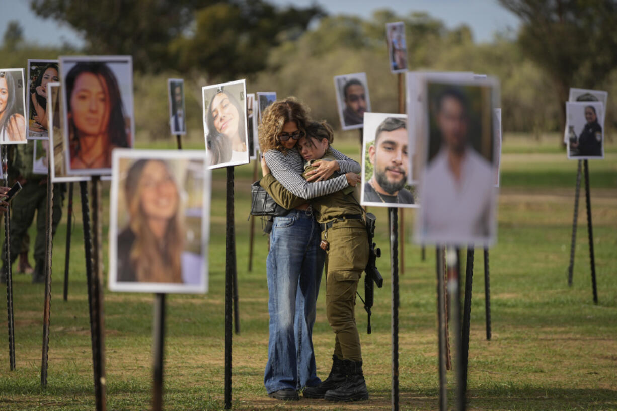 Israelis embrace next to photos of people killed and taken captive by Hamas militants during their violent rampage through the Nova music festival in southern Israel, which are displayed at the site of the event, as Israeli DJs spun music, to commemorate the October 7, massacre, near kibbutz Re&rsquo;im, Tuesday, Nov. 28, 2023.