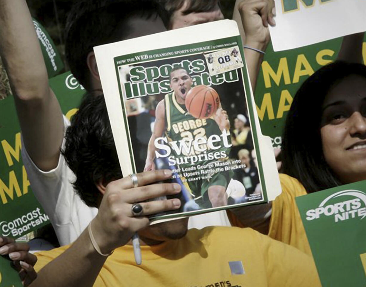 FILE - A George Mason University fan holds up a Sports Illustrated magazine at a send off for the team, March 29, 2006, in Fairfax, Va. Sports Illustrated is the latest media company damaged by being less than forthcoming about who or what is writing its stories. The website Futurism reported that the once-grand magazine used articles with &ldquo;authors&rdquo; who apparently don&rsquo;t exist, with photos generated by AI. The magazine denied claims that some articles themselves were AI-assisted, but has cut ties with a vendor it hired to produce the articles.
