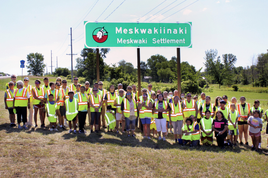 This photo taken July 13, 2022 provided by the Iowa Department of Transportation, members of the Meskwaki Nation along with employees from the Iowa Department of Transportation and Federal Highway Administration stand in front of a sign on US Highway 30 that features the Meskwaki Nation&rsquo;s own spelling of the tribe, Meskwakiinaki.