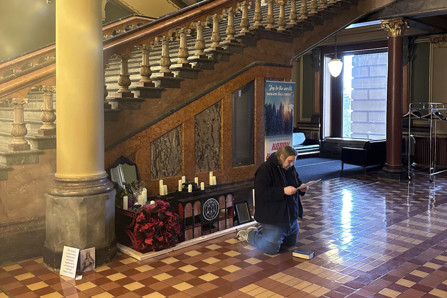 A man recites Christian prayers at a damaged Satanic display at the Iowa state Capitol on Friday, Dec. 15, 2023, in Des Moines, Iowa. The display, which has prompted outrage by some people who say it&rsquo;s inappropriate at any time but especially during the Christmas holidays, was damaged Thursday.