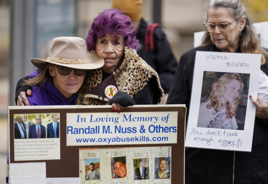 FILE - Ellen Isaacs, left, and Lee Nuss, center, both from Florida, hold each other and sing a song of remembrance for Randall M. Nuss, Lee&rsquo;s husband, during a protest with other advocates for opioid victims outside the U.S. Department of Justice, Dec. 3, 2021, in Washington. Families who lost loved ones to overdose are divided over OxyContin maker Purdue Pharma&rsquo;s plan to settle lawsuits over the toll of opioids with governments. It could provide billions to address an overdose epidemic and pay some victims. But it would also protect members of the Sackler family who own the company from future lawsuits.
