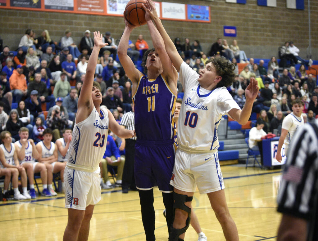 Columbia River’s John Reeder goes up for a shot attempt against Ridgefield’s Drew Krsul (23) and Colten Castro (10) during a 2A GSHL boys basketball game on Thursday, Jan. 4, 2024, at Ridgefield High School.