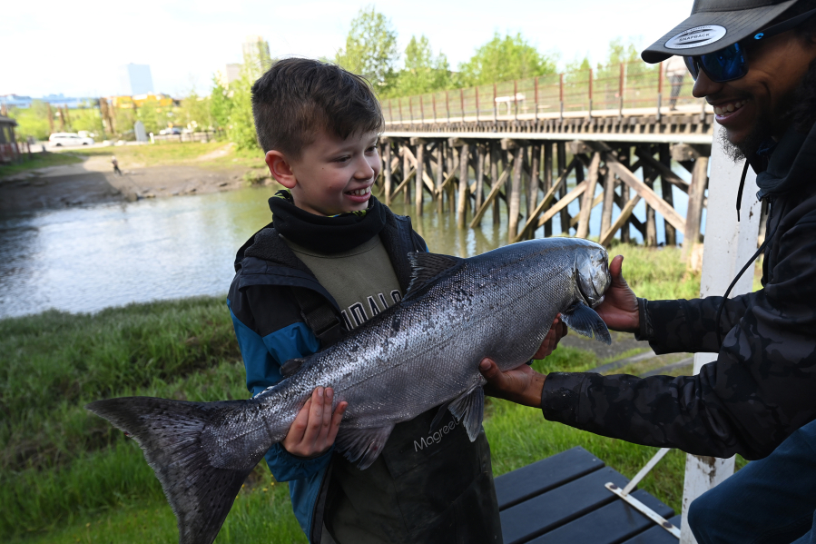 Nine-year-old Bradly Reed gets a hand from Nate Hall of The Bait Shack as he holds up a 17.45 pound king salmon he caught during an incoming tide at Ship Creek near downtown Anchorage, Alaska, on June 5, 2023.