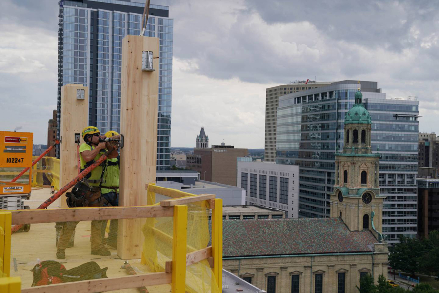 Construction workers secure an engineered wood column onto the deck of the 12th floor of the Ascent apartment building on Aug. 2, 2021, in Milwaukee. Now completed, Ascent is a 25-story tower and the world&rsquo;s tallest hybrid timber building.