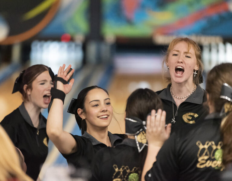 Evergreen’s Bella Curry, center, is cheered on by teammate Savannah McMurtry, right, and others after a throw Friday, Jan. 26, 2024, during the WIAA District 4 3A/4A championships at Hazel Dell Lanes.