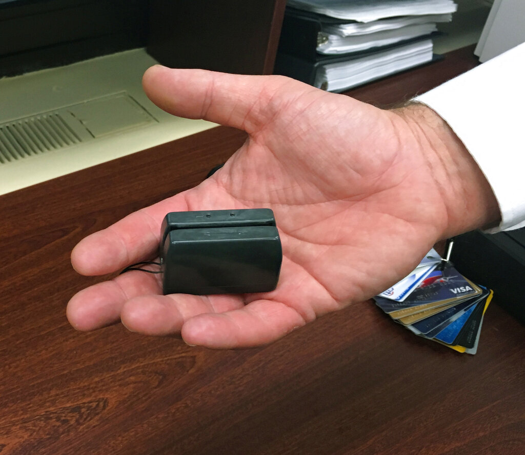 In this Dec. 17, 2015 photo, a New York City Police detective holds a credit card skimmer that was used by a street gang to copy metadata from legitimate credit cards for use in the manufacture of counterfeit cards and possibly identity theft. A new trend is emerging that shows street crews and local gangs giving up more traditional activities like gun point robberies or drug running for more white-collar varieties of crime like identity theft or credit card fraud.