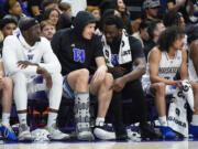 Washington center Franck Kepnang points to a new boot worn by center Braxton Meah on the bench during the second half of the team's NCAA college basketball game against Utah, Saturday, Jan. 27, 2024, in Seattle. Washington won 98-73.