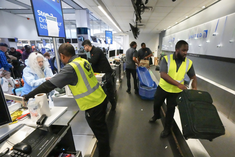 File - Agents check-in passengers and their baggage at George Bush Intercontinental Airport on Dec. 21, 2023, in Houston. On Friday, the U.S. government issues its December jobs report.